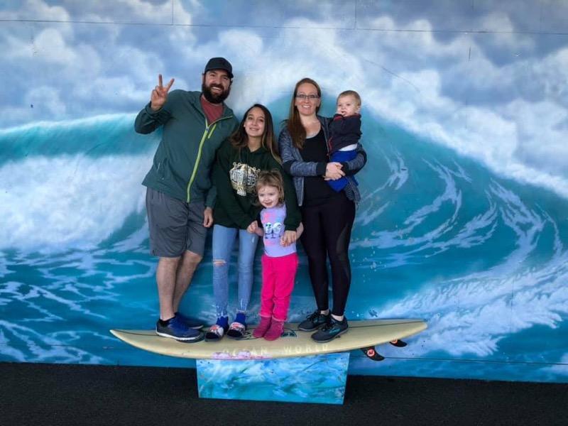 Shepherd's Dream Marketing Director Eric Smith with his family. Family is perched on a surfboard against an illustration of a wave. From left to right: Eric, his two daughters, his wife, and his baby son.