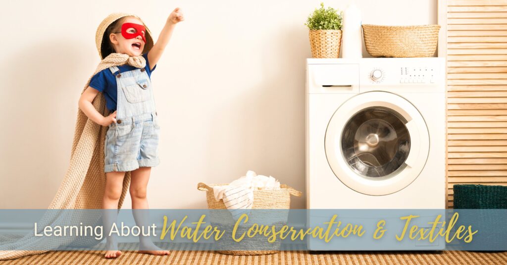 A young boy wearing a red face mask and a towel as a cape is pointing up and away next to a washing machine.