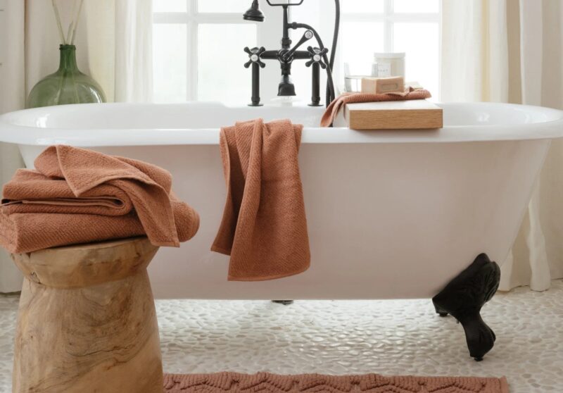 Bathroom with Coyuchi organic cotton Air Weight towels in Sedona on a white bath tub and wooden pedestal