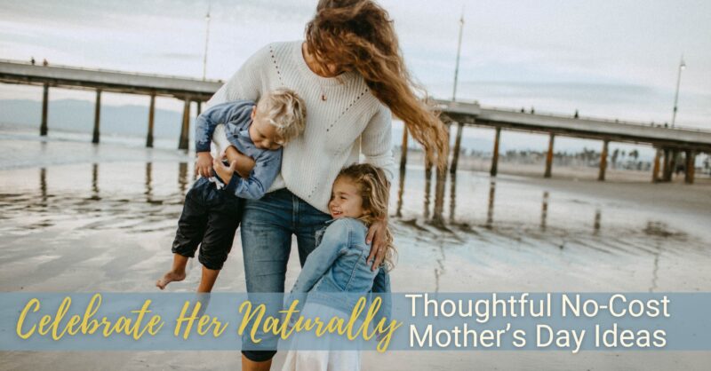 A woman holds one child while another clutches her leg as they all smile on the beach.